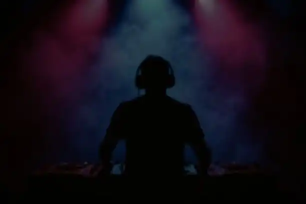DJ en la cabina iluminado por luces de colores en un ambiente con humo